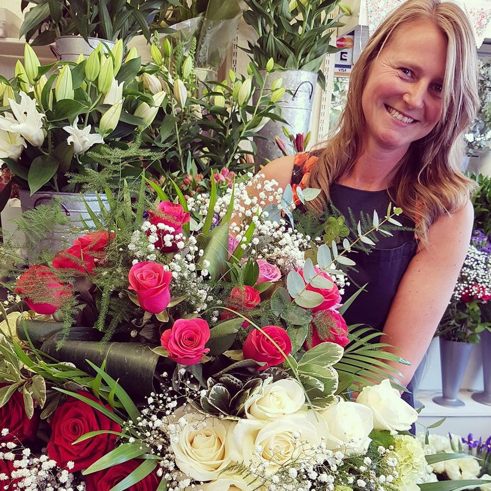 Allison holding a large, lush floral arrangement featuring red and white roses, green foliage, and white baby's breath in a flower shop.